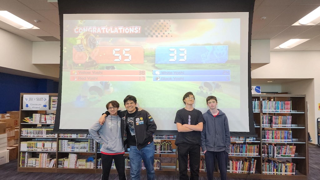 Top two teams from the 26 Mario Kart tournament stand in front of the game screen
